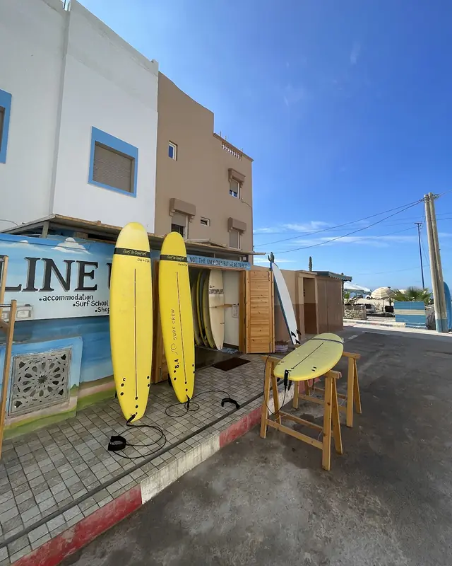 Yellow soft-top surfboards leaning against the painted LINE UP mural outside the shop