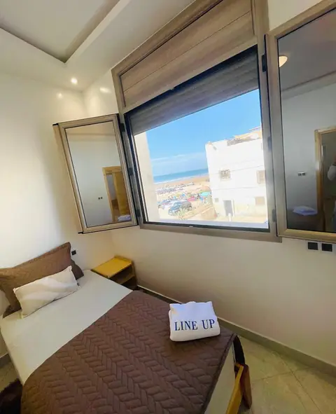 Sea-view triple room at Line Up: a bed beside a wide open window with the beach and sea outside