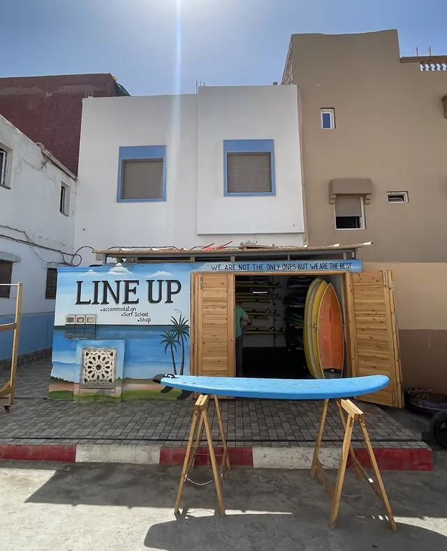 The front of Line Up: white house with blue window frames, the shop doors open under the LINE UP mural, a blue surfboard on trestles