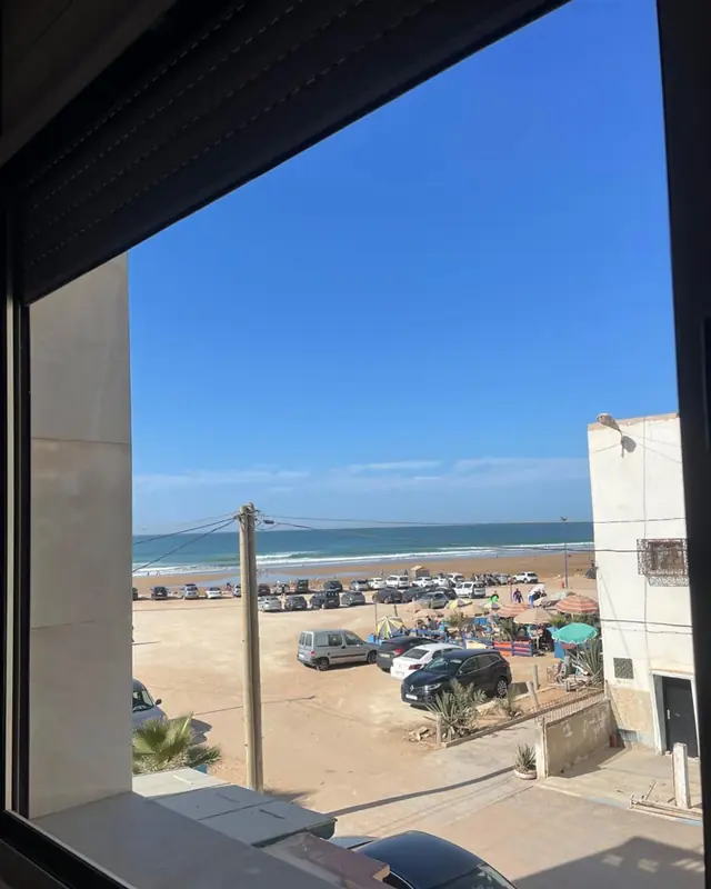 A dark window frame in a sea-view room at Line Up, looking over the beach car park to the sand and the sea